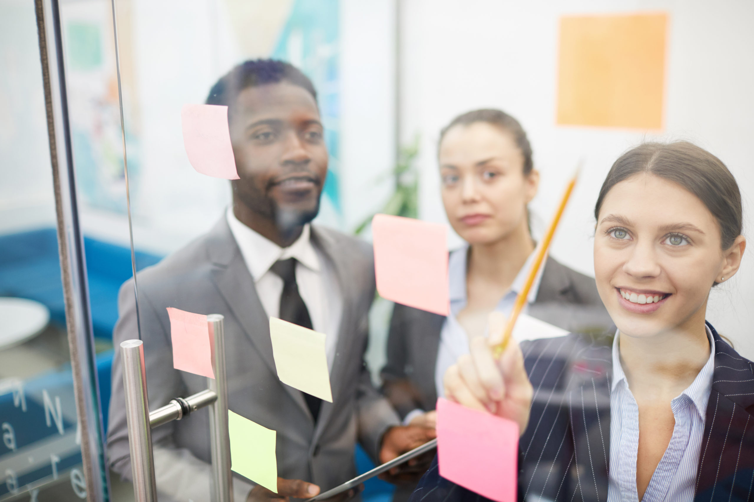 Multi-ethnic group of business people planning startup project placing sticky notes on glass wall, copy space